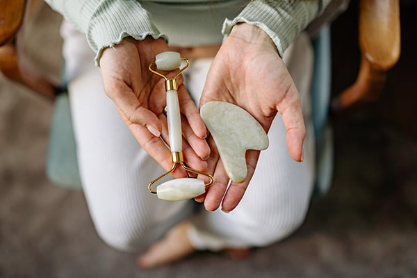 Person holding a face roller and a gua sha